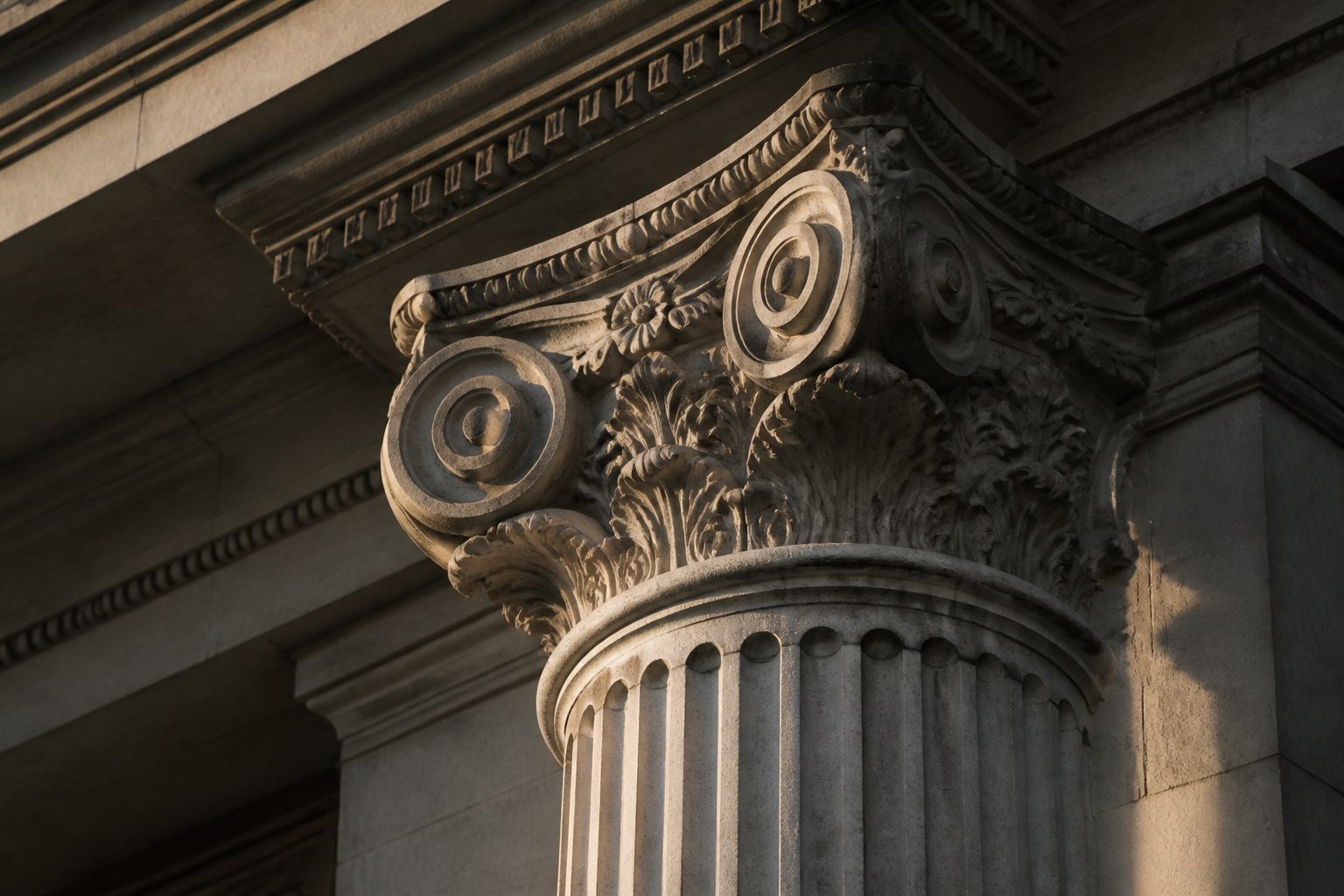 Weathered Greek and Roman limestone column capital, Ionic scrolls and a fluted shaft in raking light